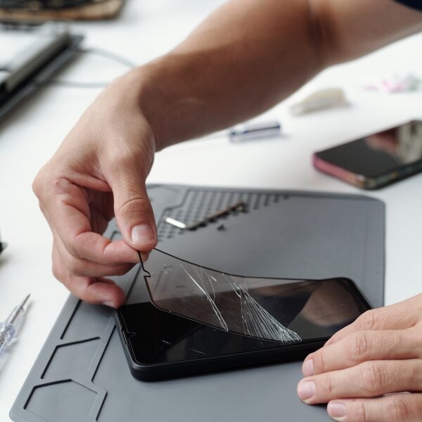 Fixing Cracked Smartphone Screen with Precision Tooling Close-up of hands repairing cracked smartphone screen using specialized tools on tech workbench. Many small components and electronic devices are scattered around