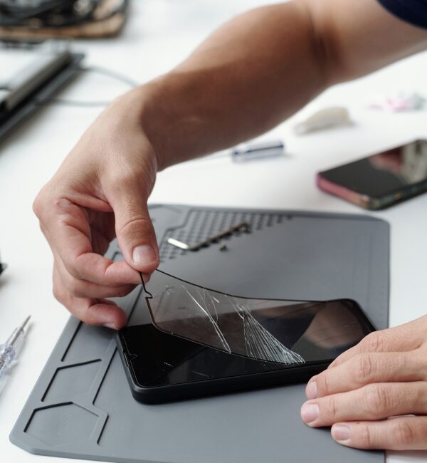 Fixing Cracked Smartphone Screen with Precision Tooling Close-up of hands repairing cracked smartphone screen using specialized tools on tech workbench. Many small components and electronic devices are scattered around